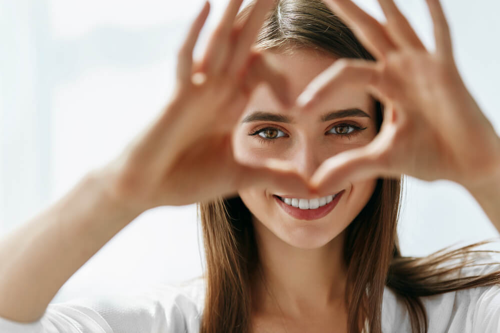 Young woman looking through heart shape made with her fingers
