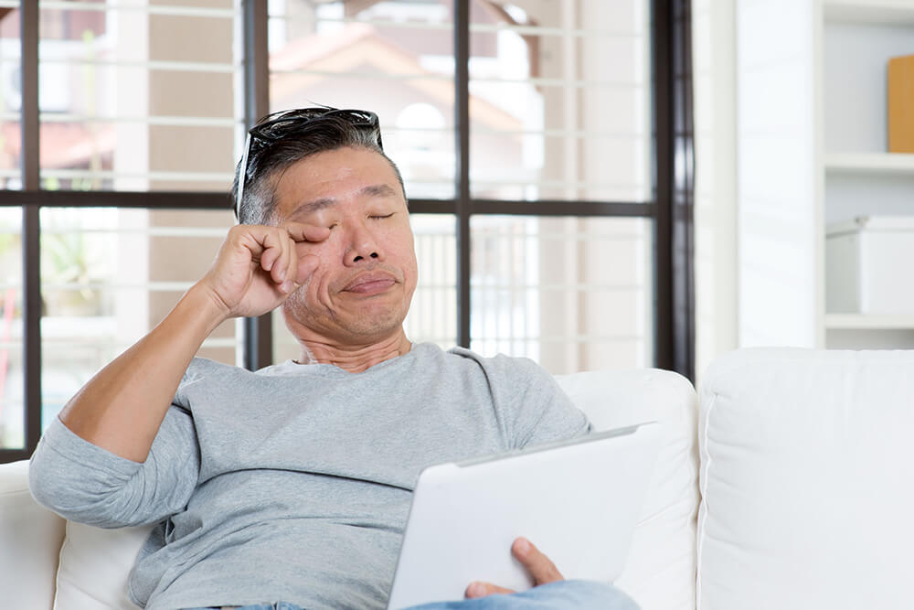 Man on couch rubbing his eye