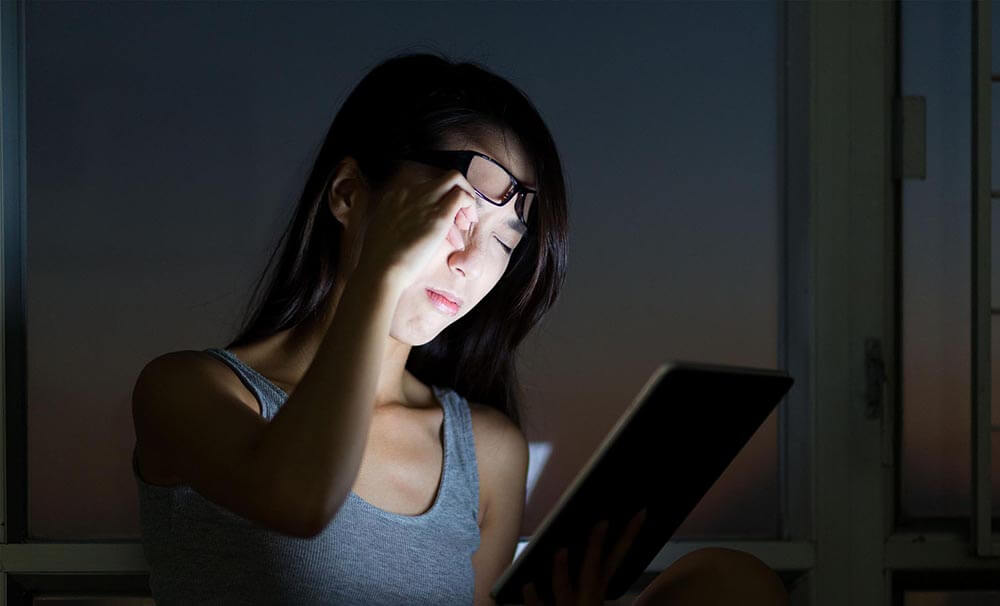 Tired young woman reading tablet at night